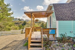 Une terrasse en bois avec des marches menant à une zone abritée, un panneau indicateur et une vue sur des maisons en arrière-plan.