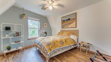 A bedroom with a bed, a desk, a bookshelf, a ceiling fan, and a window.