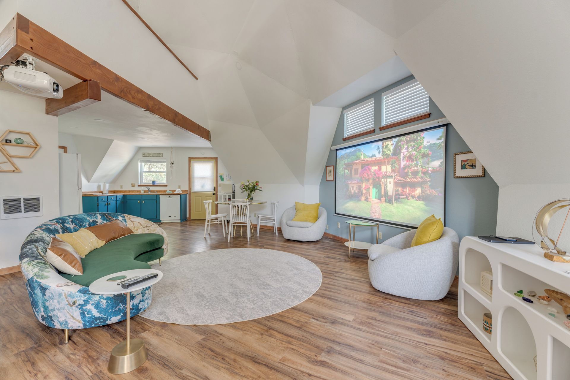 A spacious loft with a kitchen, dining area, and a large screen for entertainment.