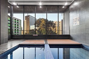 En modern inomhuspool med väggar av genomskinligt glas, ett kaklat golv och utsikt över stadens byggnader.