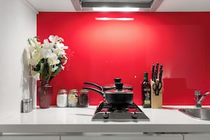 A kitchen with a red backsplash, a gas stove, a pot on the stove, a vase with flowers, and various kitchen utensils. - CBD Sanctuary | 2BR, Tram, Pool, Spa, Sauna & Gym (Melbourne)