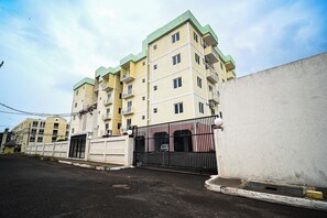 Un edificio residencial de varios pisos con balcones, entrada protegida por una reja y cielo despejado.