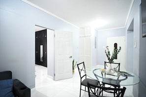 Un comedor moderno con una mesa de vidrio, sillas negras, un jarrón blanco con plantas y una puerta cerrada al fondo.