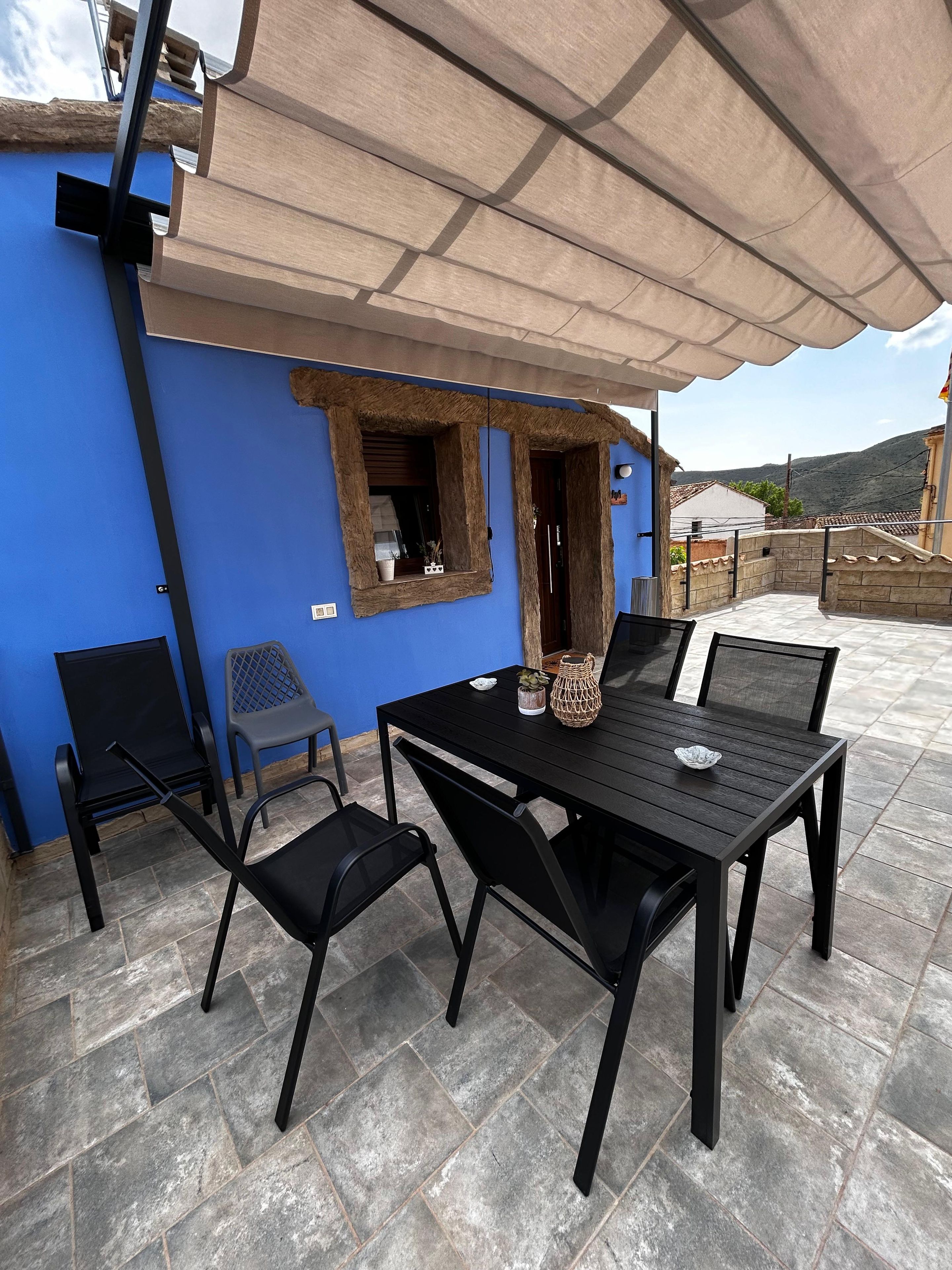 Een terras buiten met een tafel en stoelen, een overdekt gedeelte en uitzicht op het omliggende landschap.