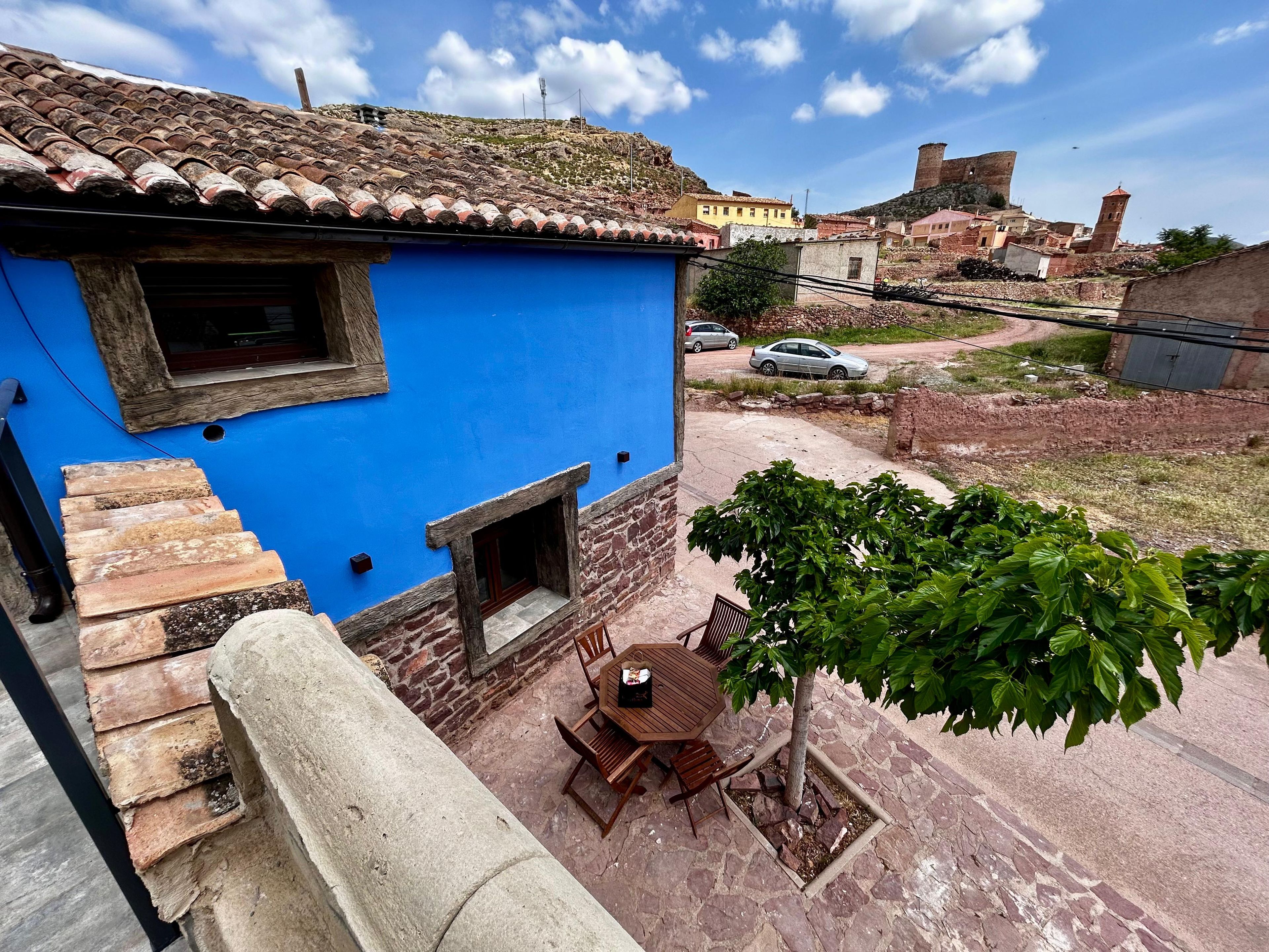 A blue building with a stone staircase, a small window, and a table with chairs outside.