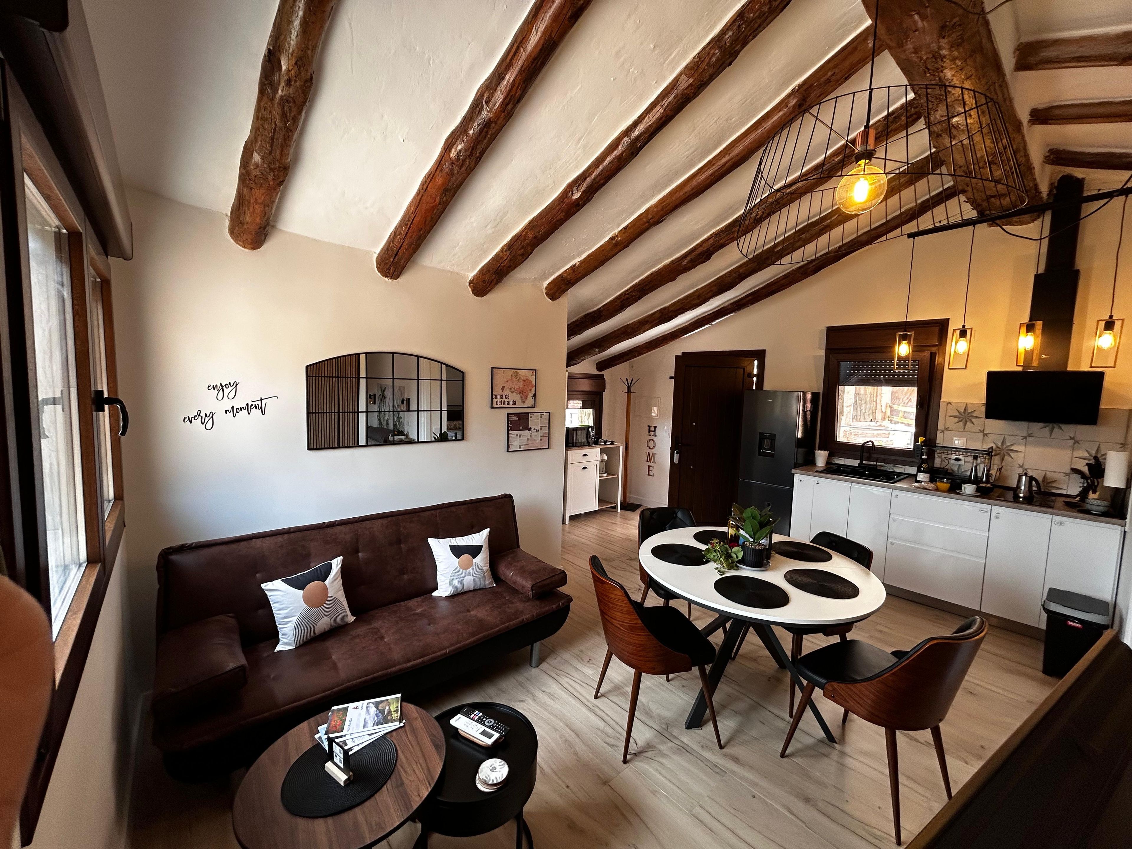 A modern living room with a brown sofa, a round dining table, and a kitchen in the background.