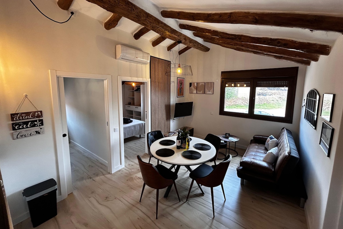 Een gezellige kamer met een eettafel, stoelen, een bank en een raam met uitzicht.