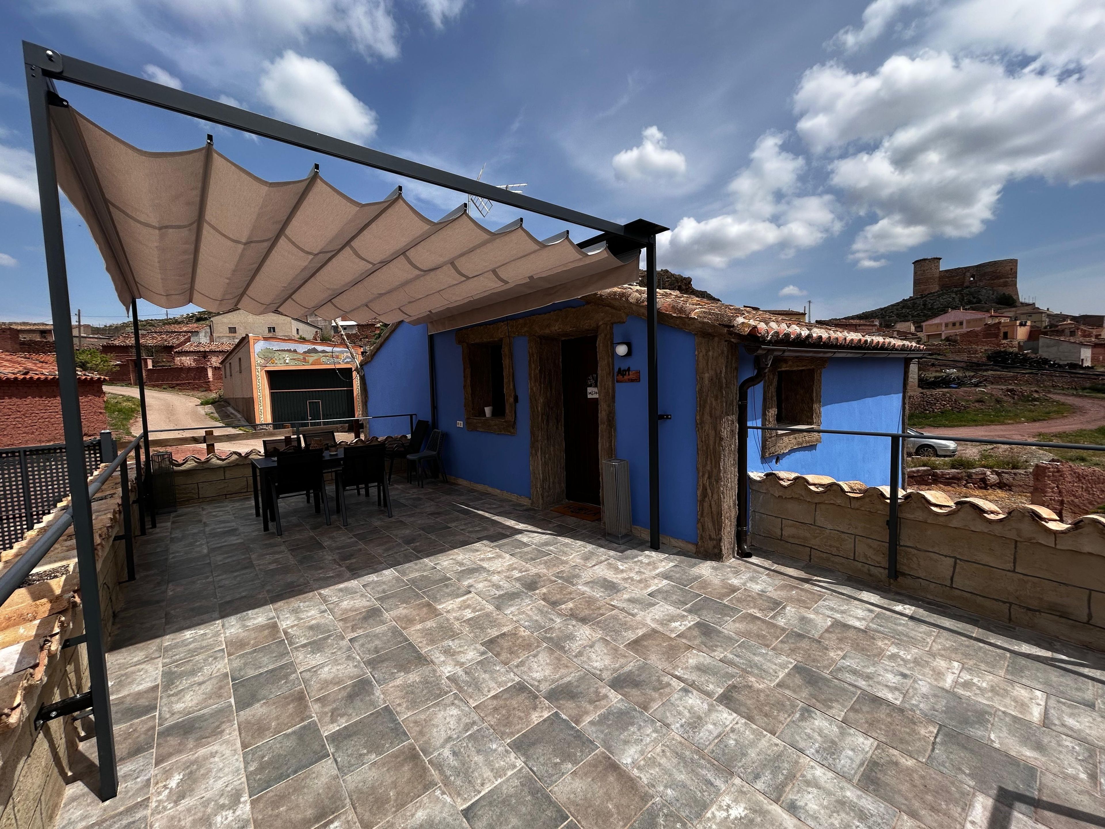 A patio area with a table and chairs, a covered seating area, and a view of the surrounding neighborhood.