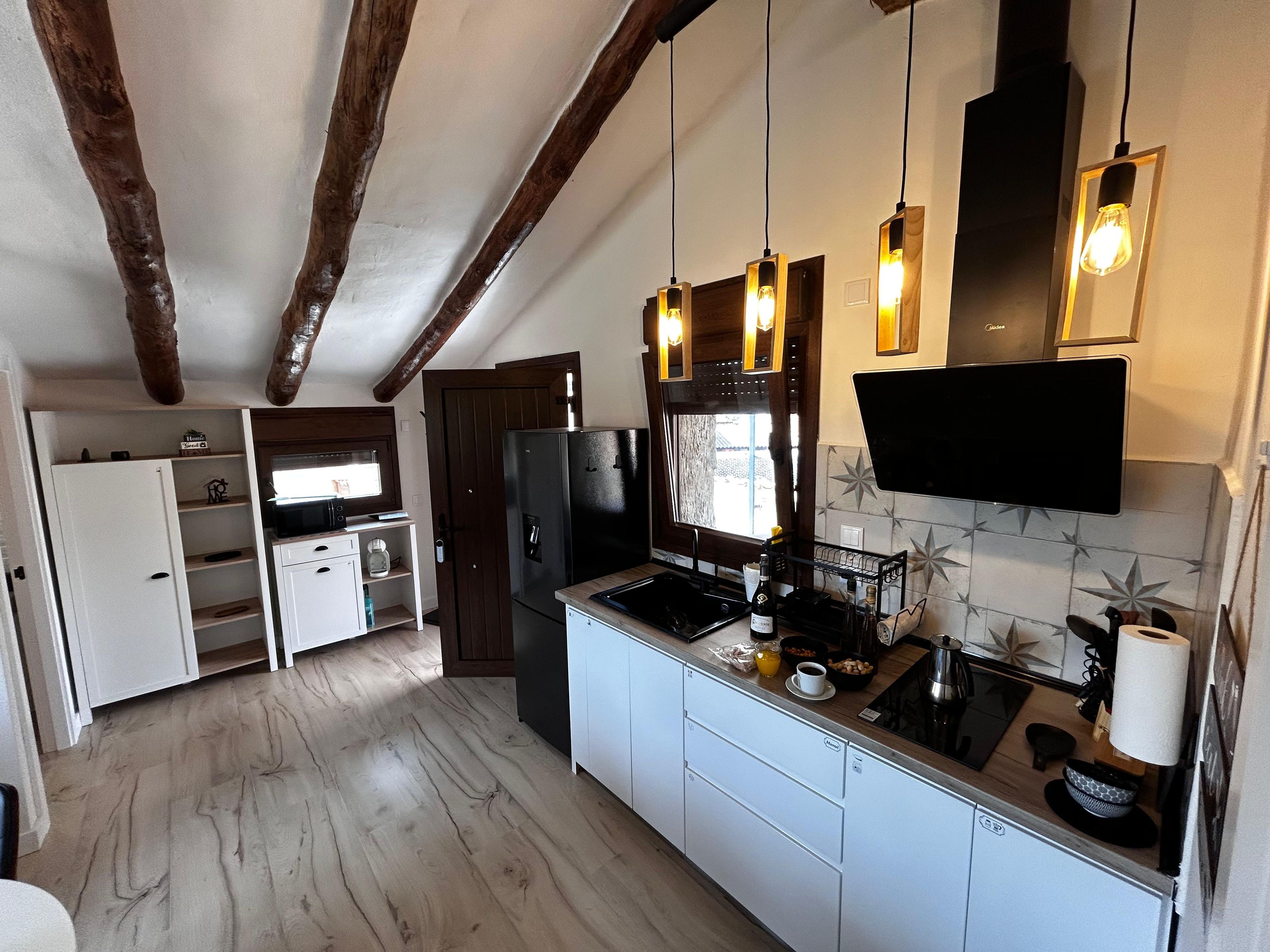 Cocina compacta con refrigerador integrado, microondas y estufa. Hay lámparas colgantes y un televisor de pantalla plana montado en la pared.
