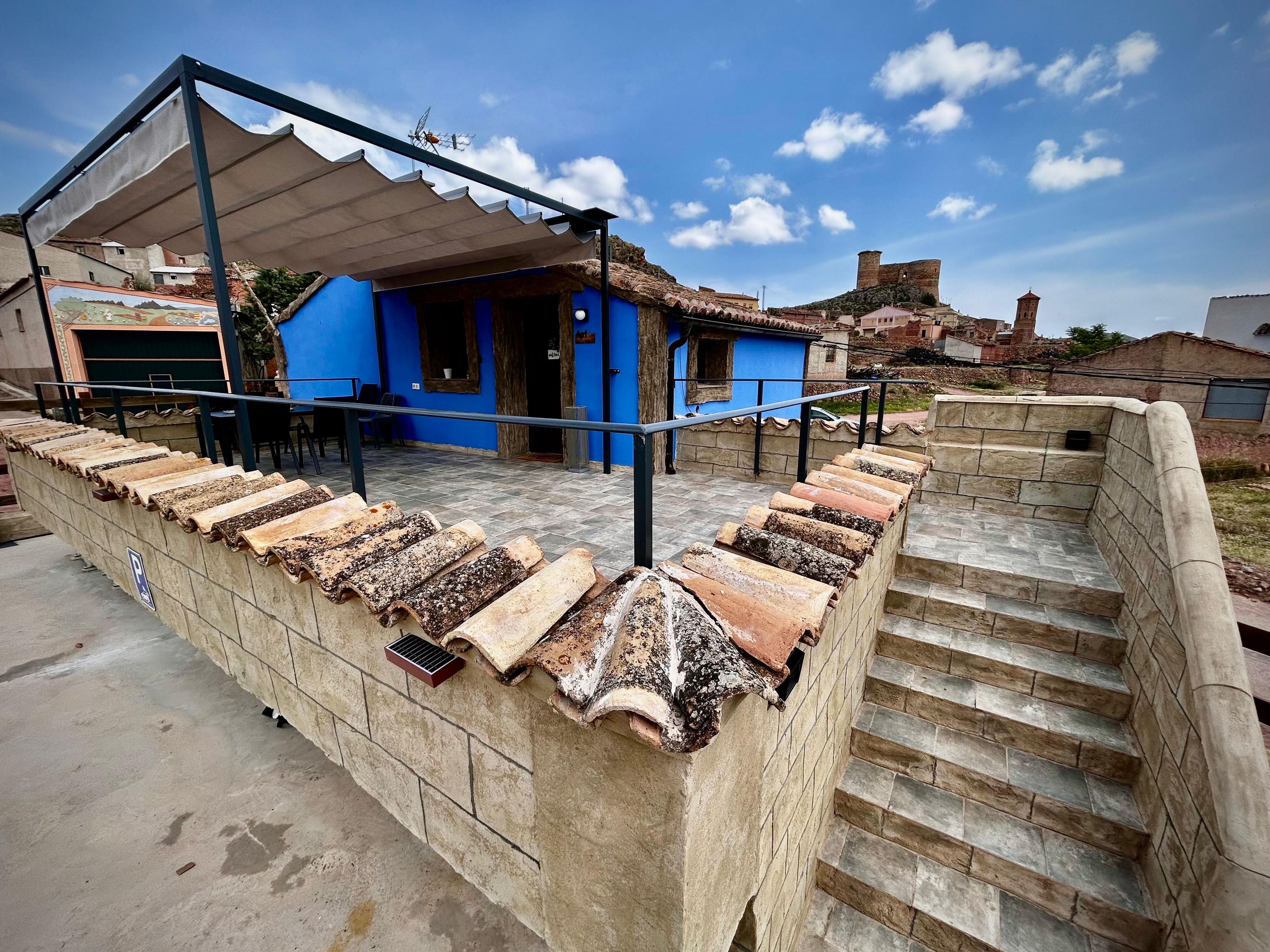 A building with a blue exterior, a covered outdoor seating area, and a stone staircase leading to a higher level.