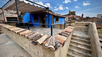 A building with a blue exterior, a covered outdoor seating area, and a stone staircase leading to a higher level.