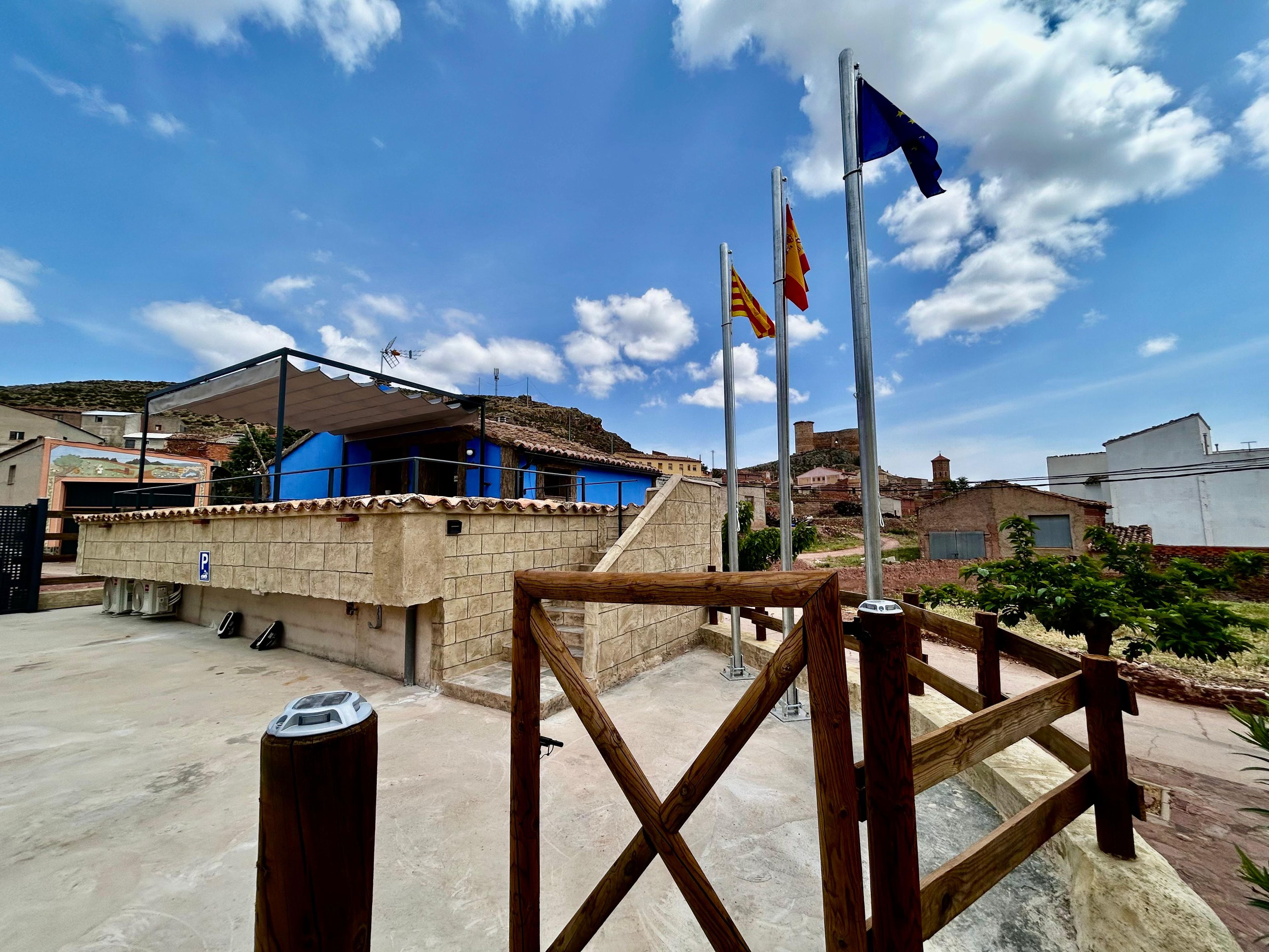 A building with a blue facade, a flagpole with multiple flags, and a clear sky.