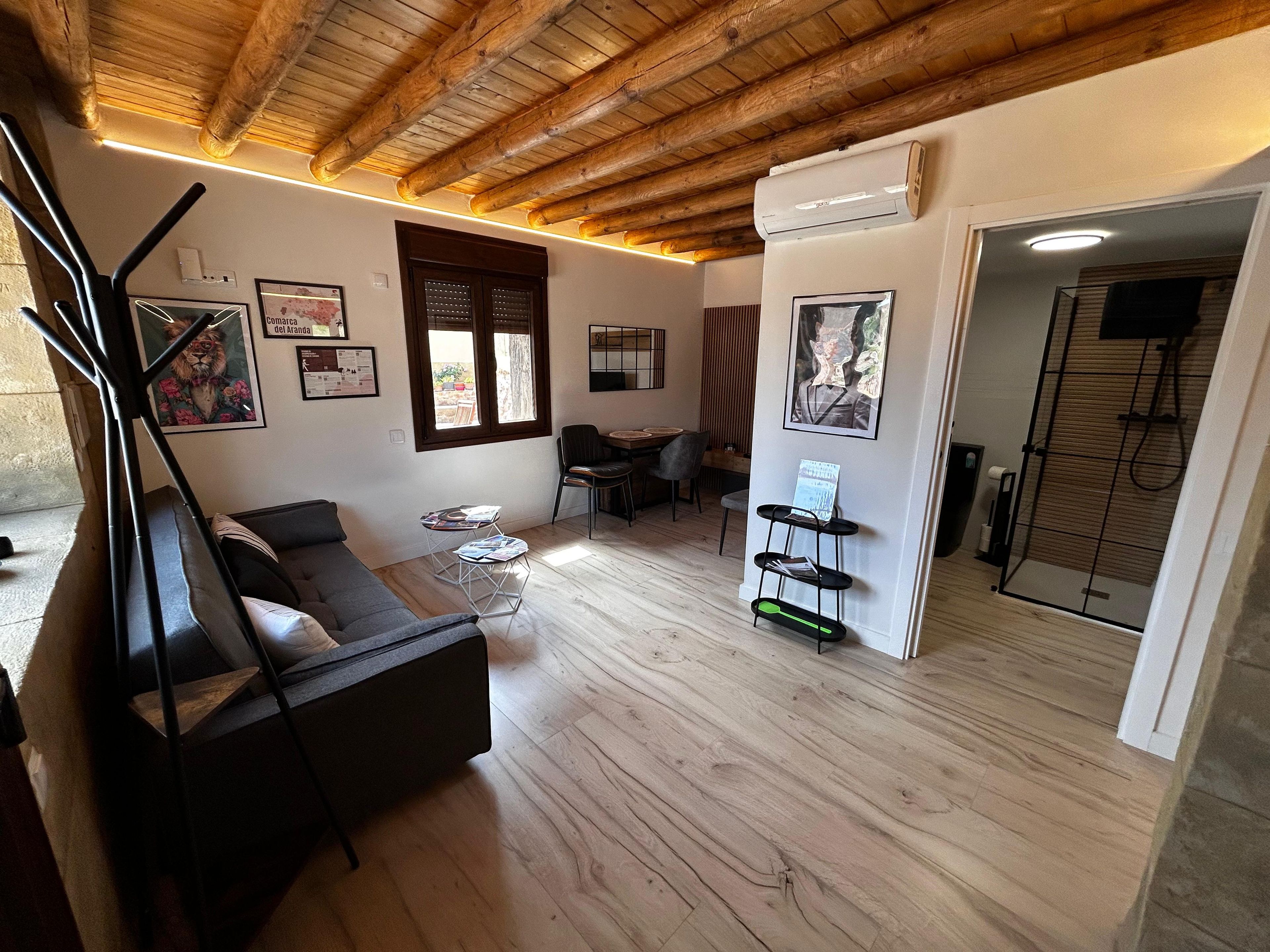 A modern living room with a wooden ceiling, a sofa, a coffee table, and a small dining area.