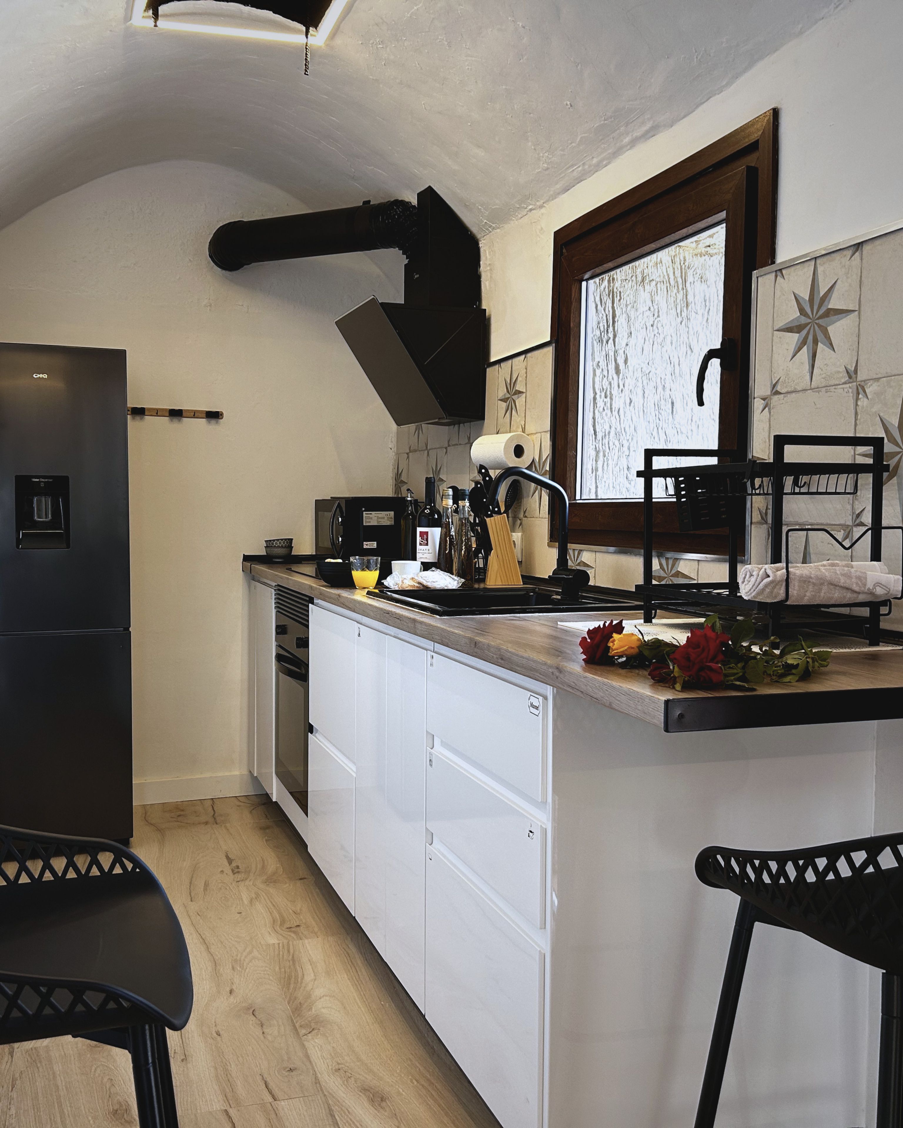 A compact kitchen with a built-in refrigerator, a sink, and a window with a star-patterned backsplash.