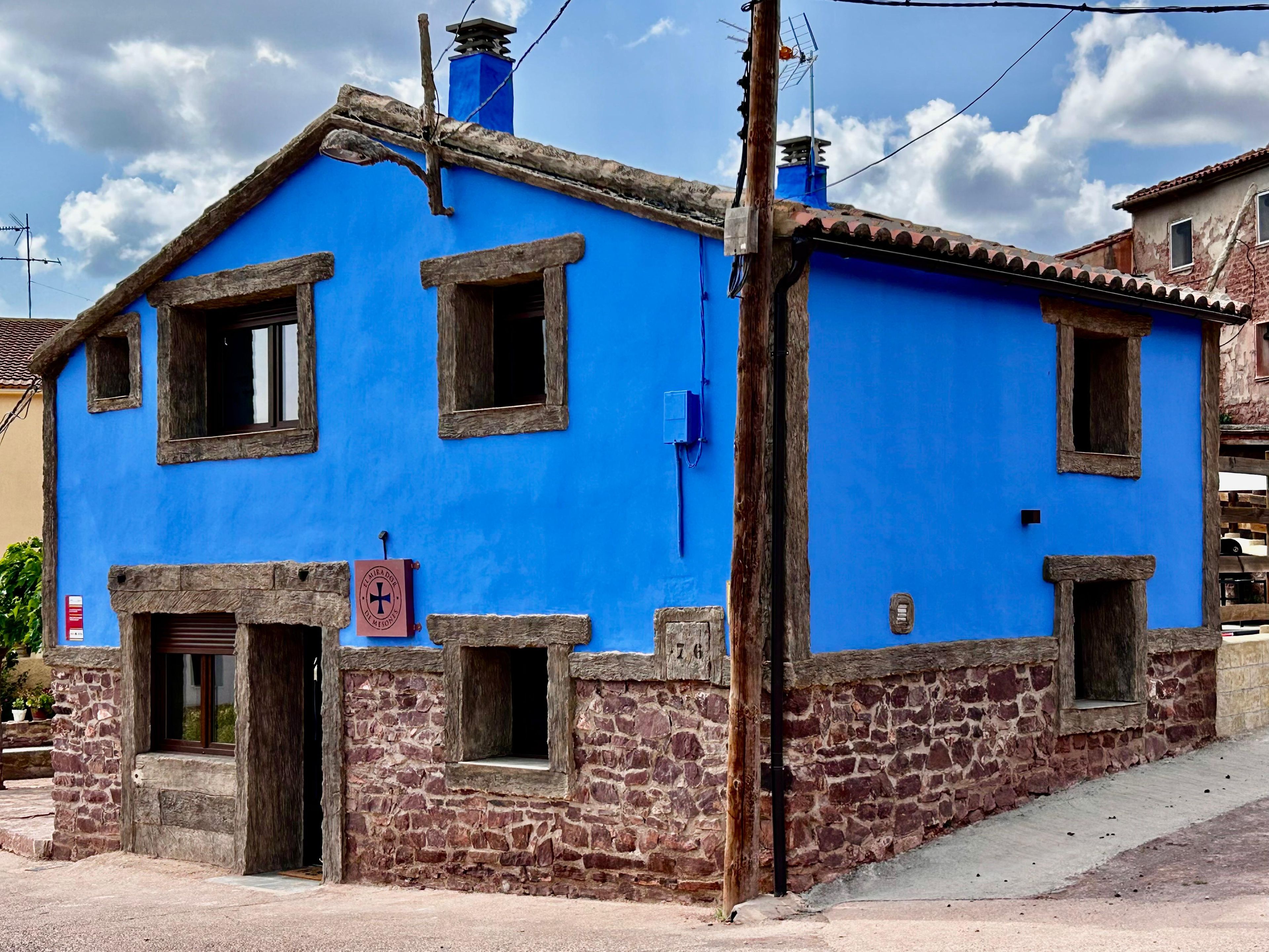 Een gebouw met twee verdiepingen, een blauwe gevel en een stenen basis, met meerdere ramen en een duidelijke deur.