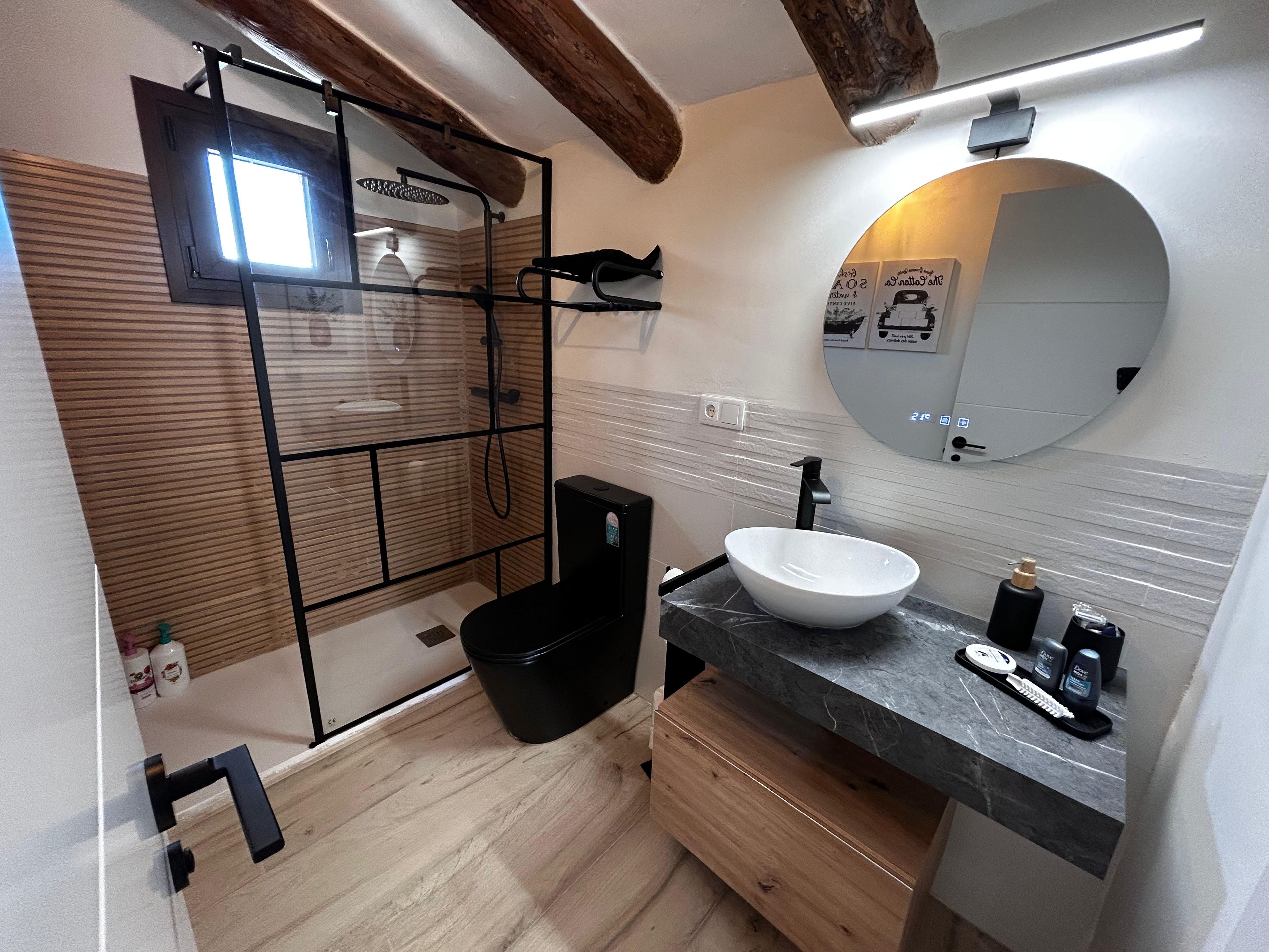 Een badkamer met een houten vloer, een witte wastafel, een zwart bad en een spiegel met een ronde lijst.