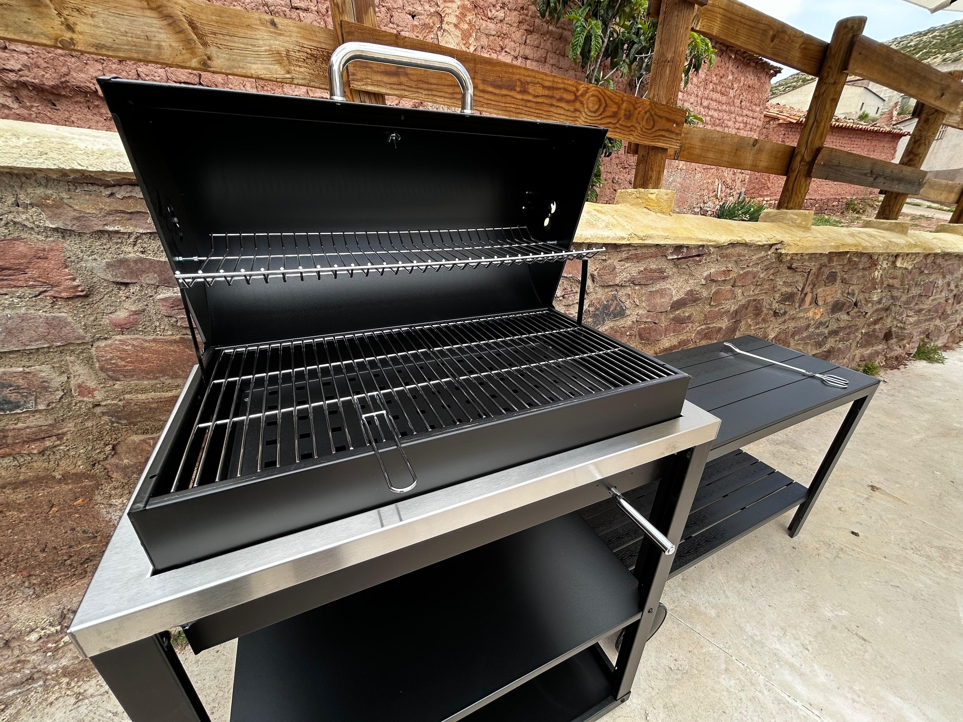 Una parrilla portátil con rejilla de metal, un asa y un estante para guardar alimentos.