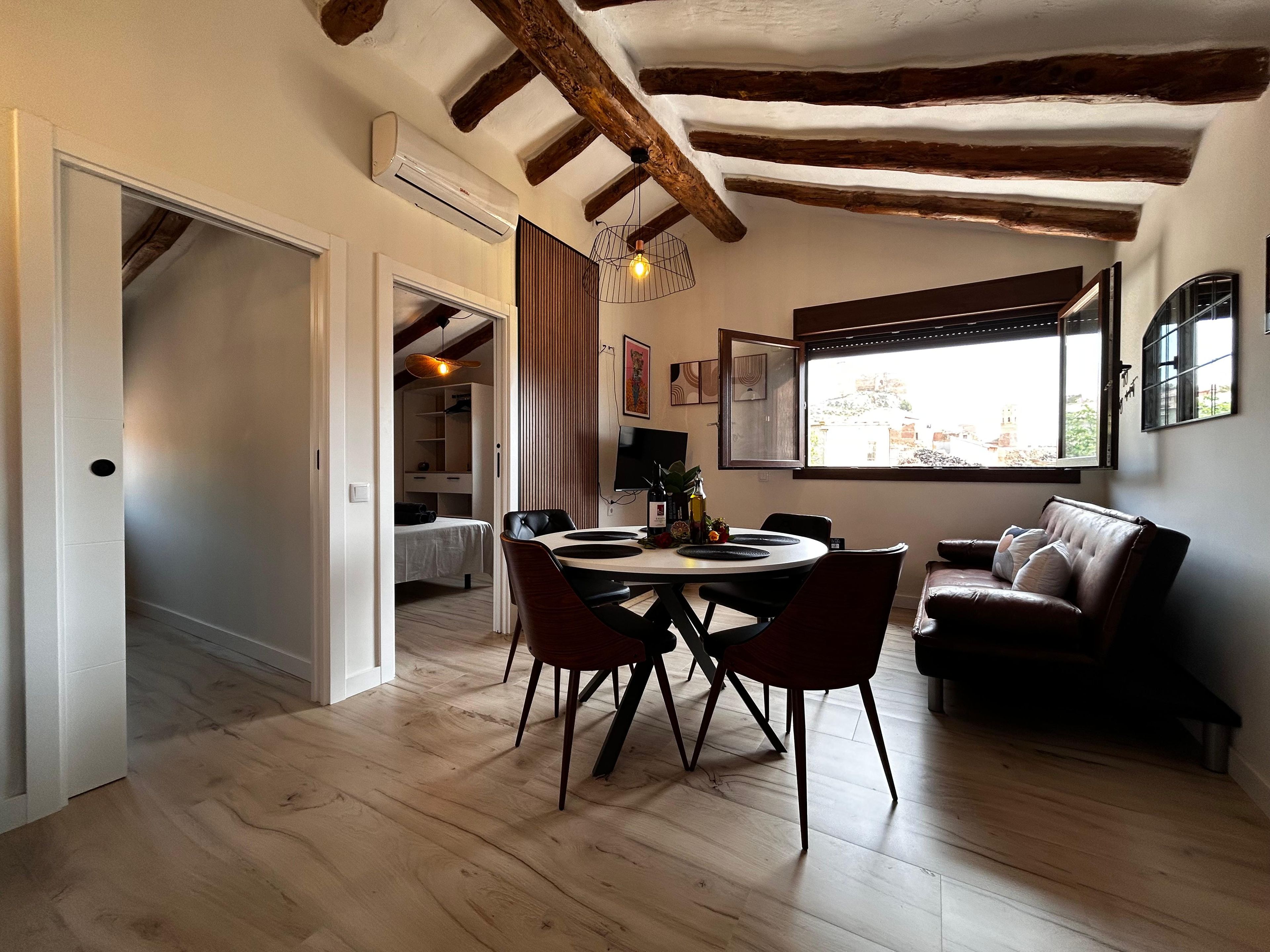 A dining area with a wooden table and chairs, a sofa, and a window with a view.