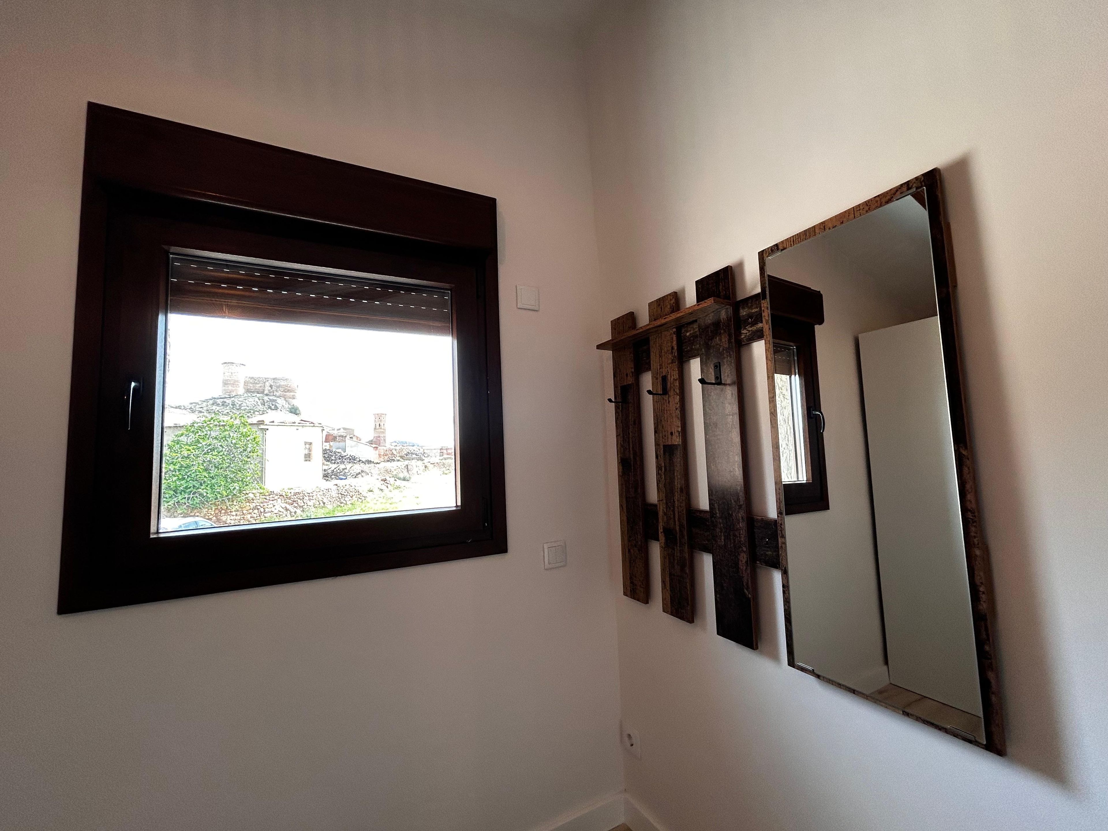 Um quarto com janela, espelho e prateleira de madeira.