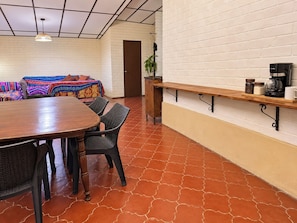 Un coin repas avec une table et des chaises en bois, un banc avec une machine à café, et un mur en briques blanches.
