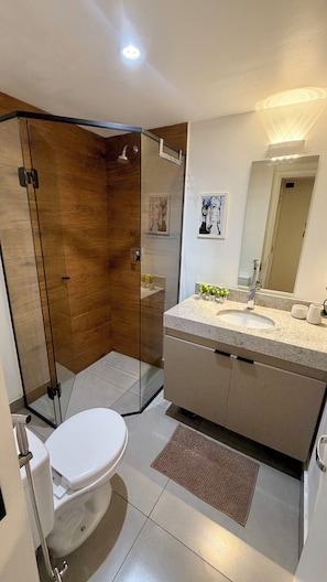 Ein modernes Badezimmer mit einer gläsernen Dusche, einer Toilette, einem Waschbecken mit Spiegel und einer kleinen Topfpflanze auf der Ablagefläche.