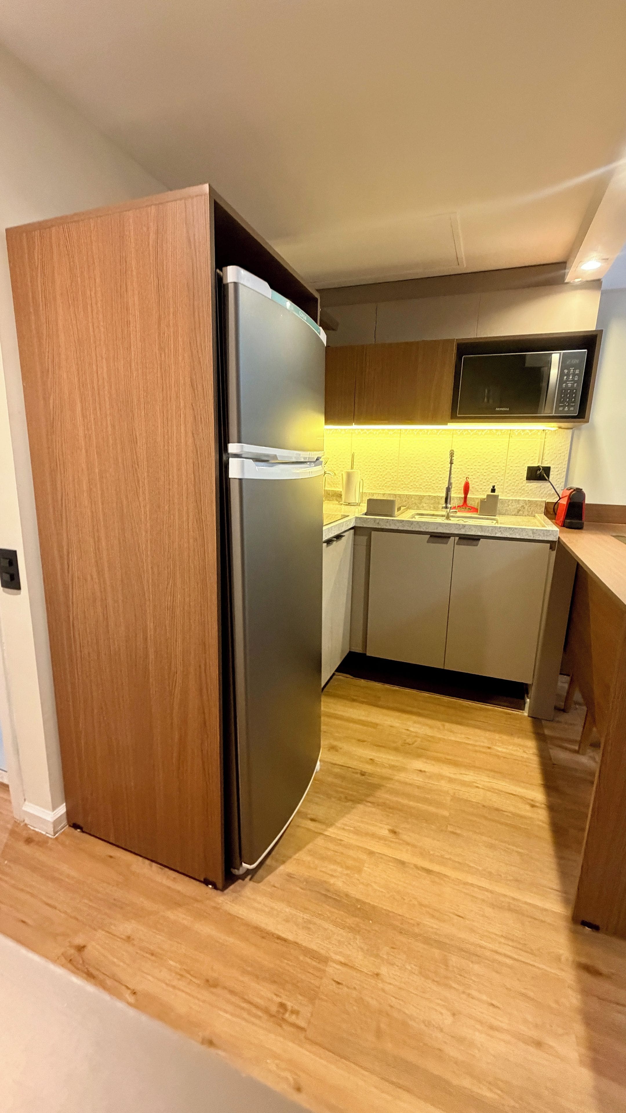 Eine kleine Küche mit einem integrierten Kühlschrank, einer Mikrowelle und einem Spülbecken.