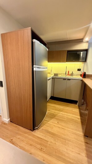Eine kleine Küche mit einem integrierten Kühlschrank, einer Mikrowelle und einem Spülbecken.
