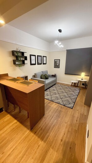 Ein modernes Wohnzimmer mit einem Holzespeisetisch, einem grauen Sofa und einem gemusterten Teppich.