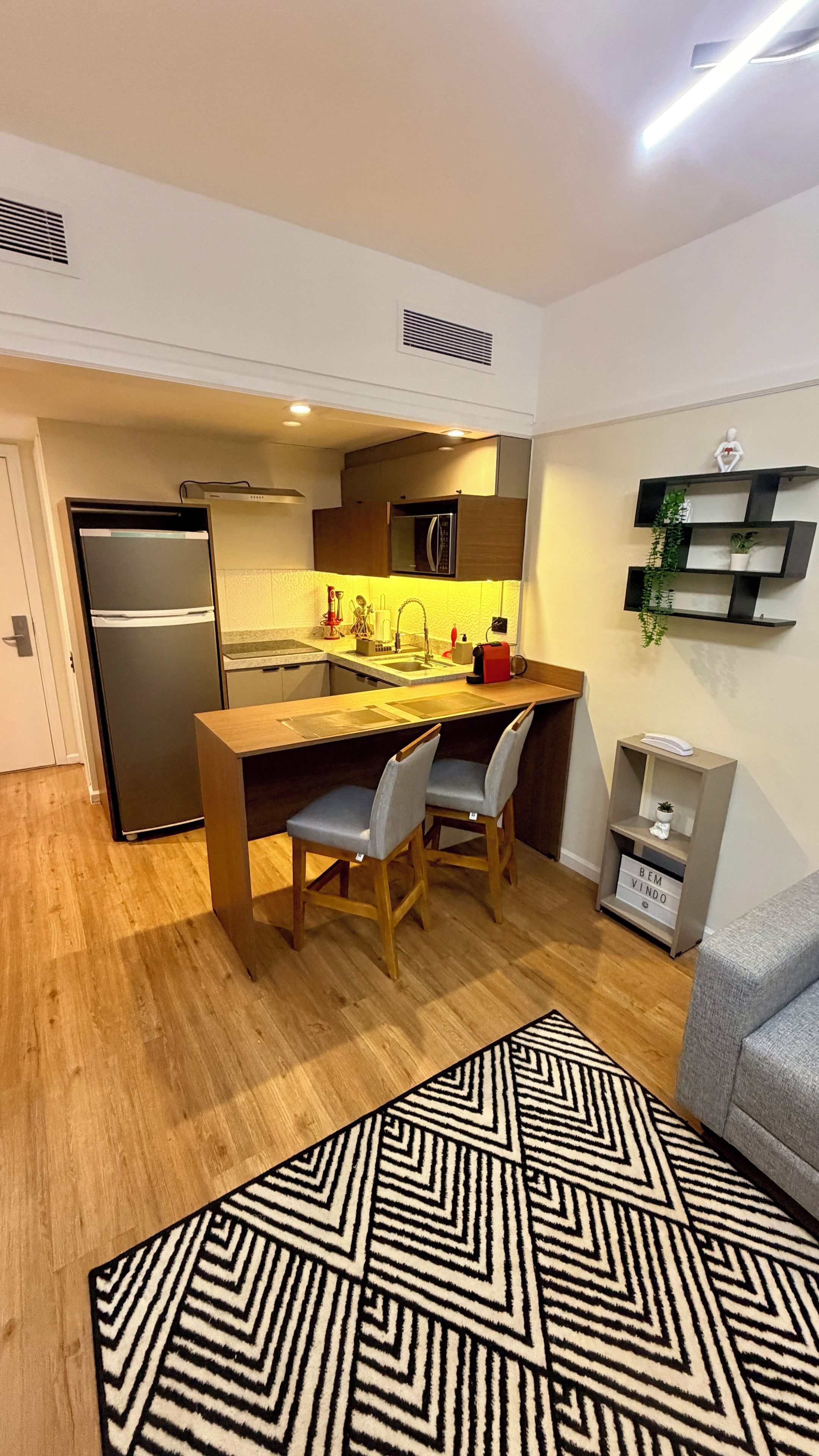 A compact kitchen with a refrigerator, a microwave, and a sink. There are two chairs and a small table.