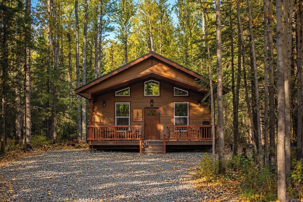 Una baita con rivestimento in legno, un portico e un vialetto sterrato circondato da alberi.