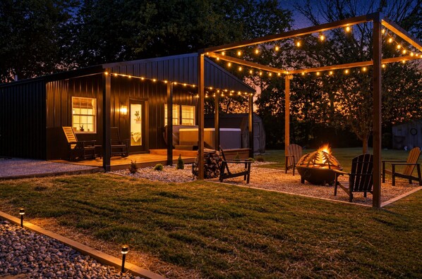 A rustic outdoor patio with a fire pit, seating, and string lights.