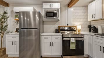 A modern kitchen with stainless steel appliances, white cabinetry, and wooden beams.