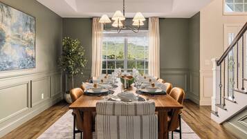 A dining room with a wooden table set for six, a chandelier, and a large window with curtains.
