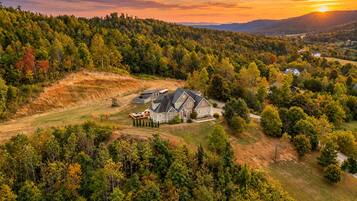 A residential area with a large house surrounded by dense forest, a playground, and a clear view of the sunset.