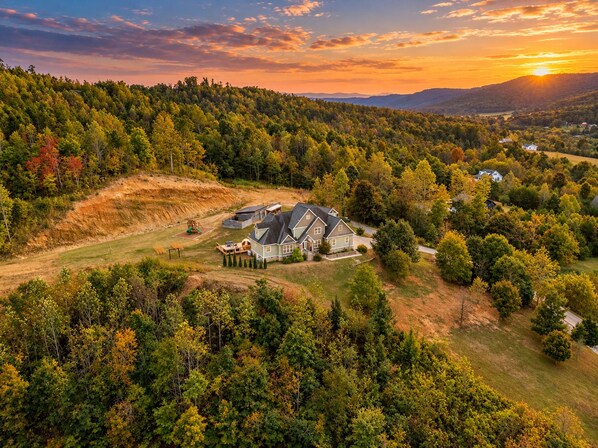 A residential area with a large house surrounded by dense forest, a playground, and a clear view of the sunset. - Private Estate • Hot Tub • Sauna • Game Room • Theater • Gym • Saloon • Mtn View (Trenton)