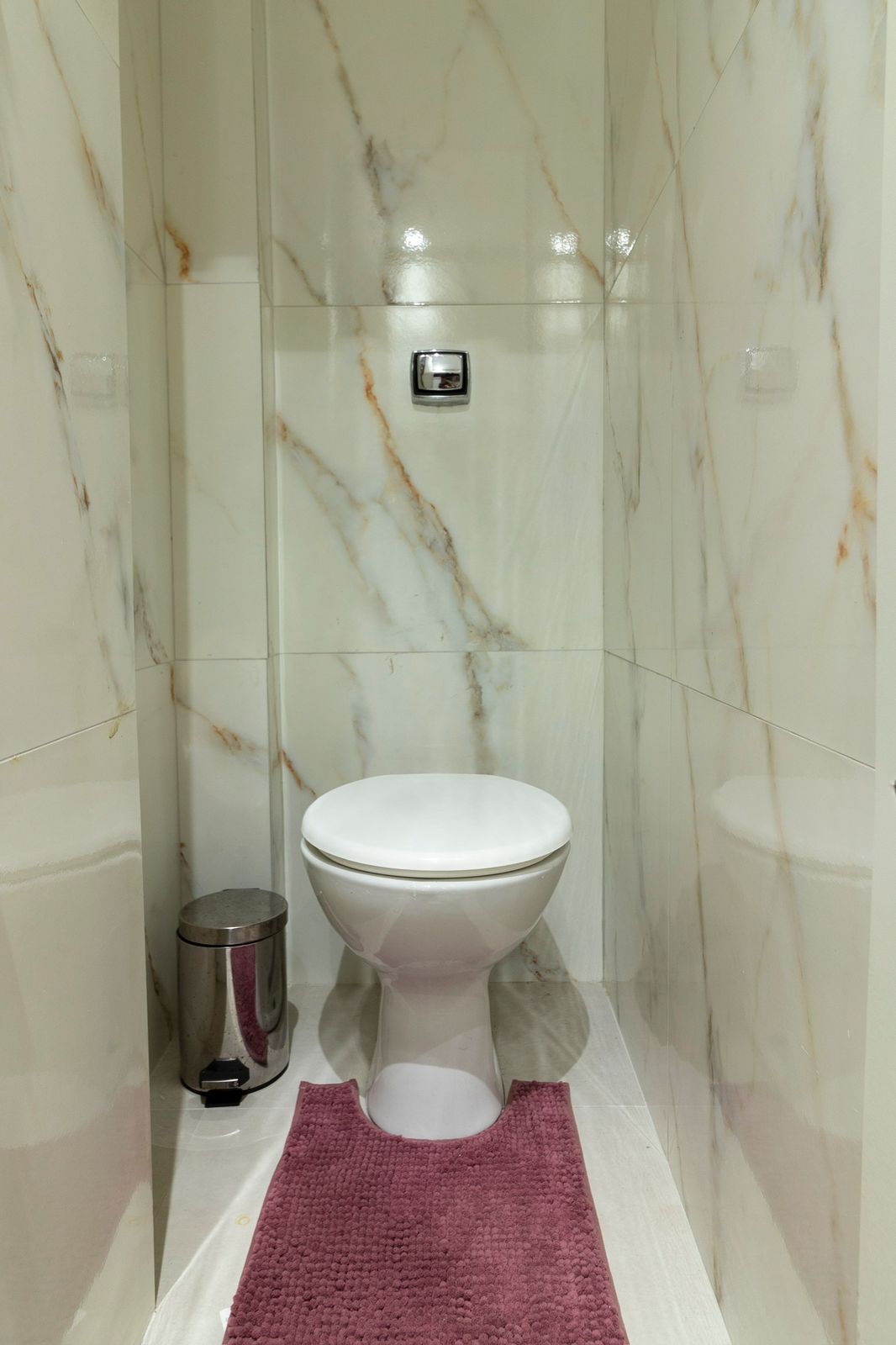 A bathroom with a toilet, a trash bin, and a marble wall.