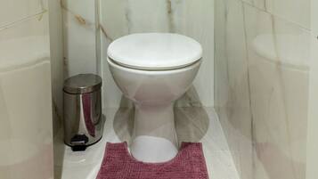 A bathroom with a toilet, a trash bin, and a marble wall.