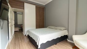 Un dormitorio con una cama, una silla, un armario y un televisor.