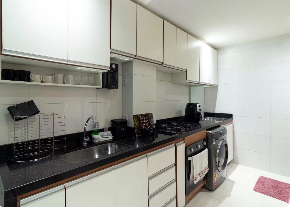 A modern kitchen with white cabinets, a black countertop, a coffee maker, a kettle, and a washing machine.