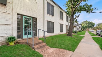 A two-story residential building with a green door, a small front yard, and a sidewalk.