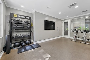 A gym with a wall-mounted rack holding kettlebells and dumbbells, a treadmill, and stationary bikes.