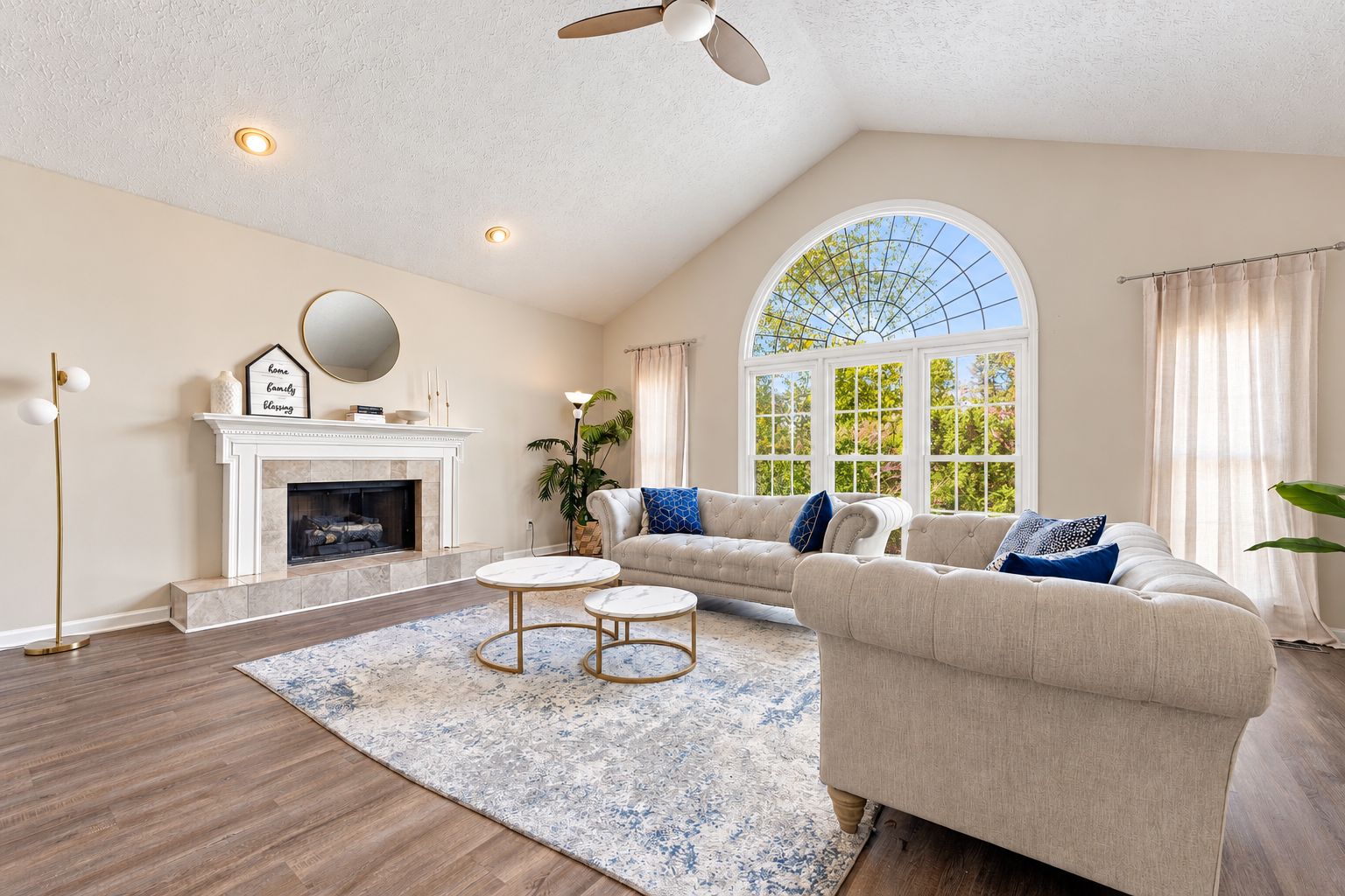 Un salon spacieux avec une cheminée, une grande fenêtre et un ventilateur de plafond.