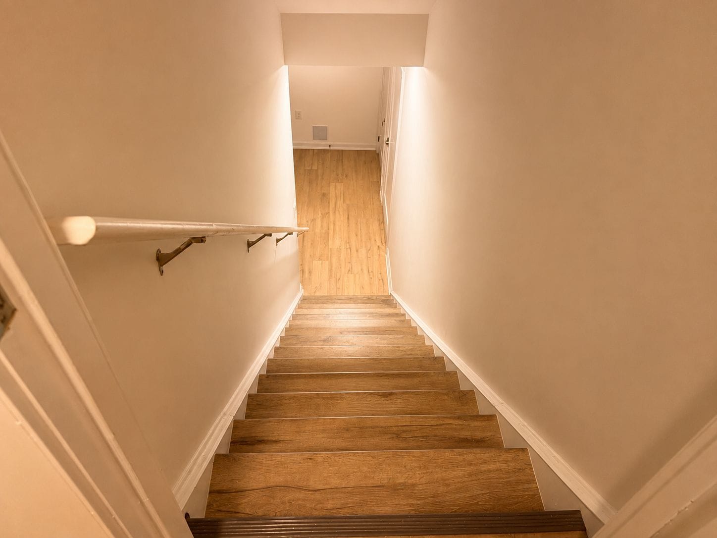 A staircase with wooden steps and white walls, leading to a landing with a light fixture.