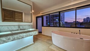Un baño moderno con una bañera grande, un tocador de mármol y un ventanal con vistas a la ciudad.