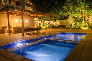 Una piscina con borde de azulejos, rodeada por un porche cubierto con sillas y una mesa.