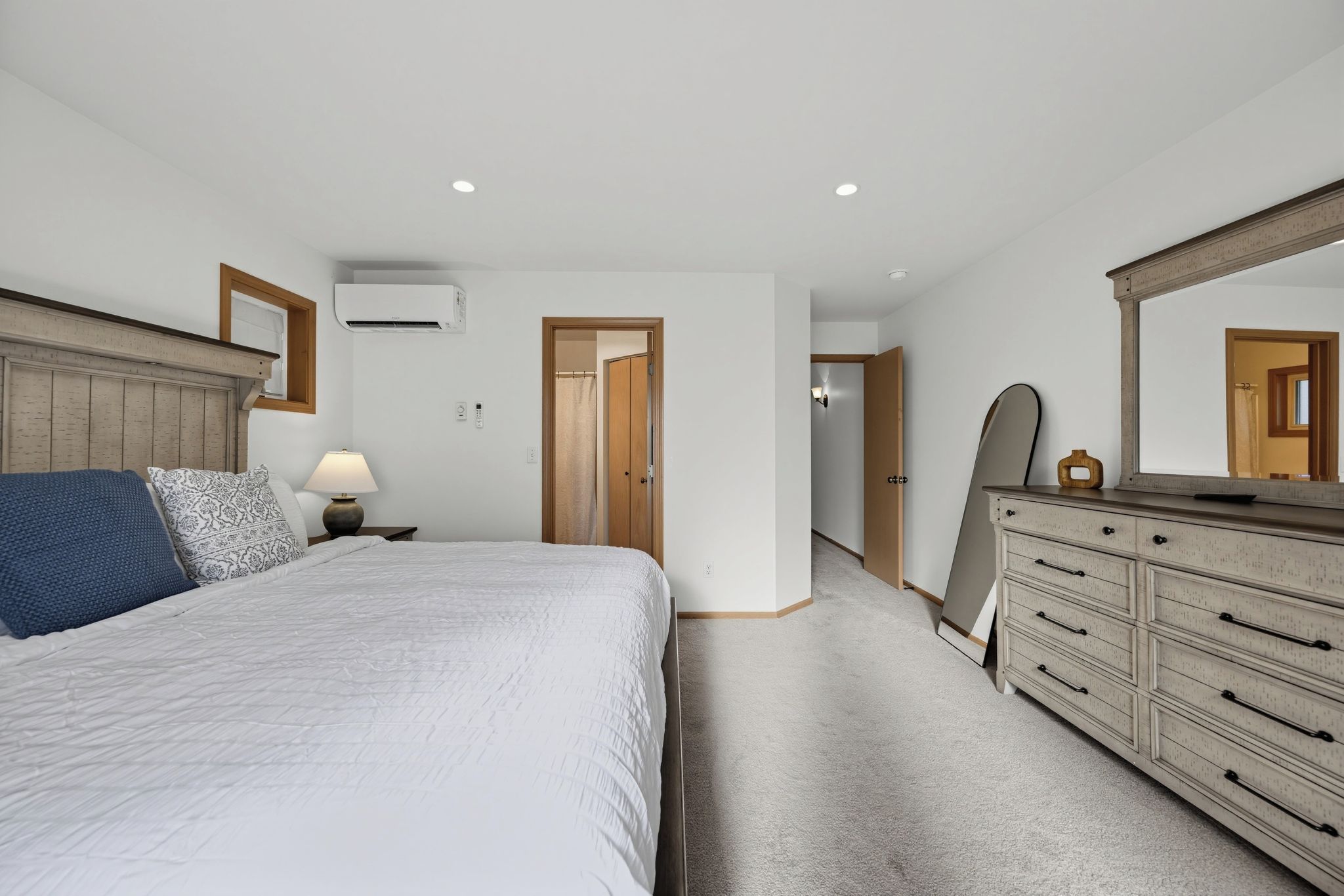 A bedroom with a bed, dresser, mirror, and an air conditioning unit.
