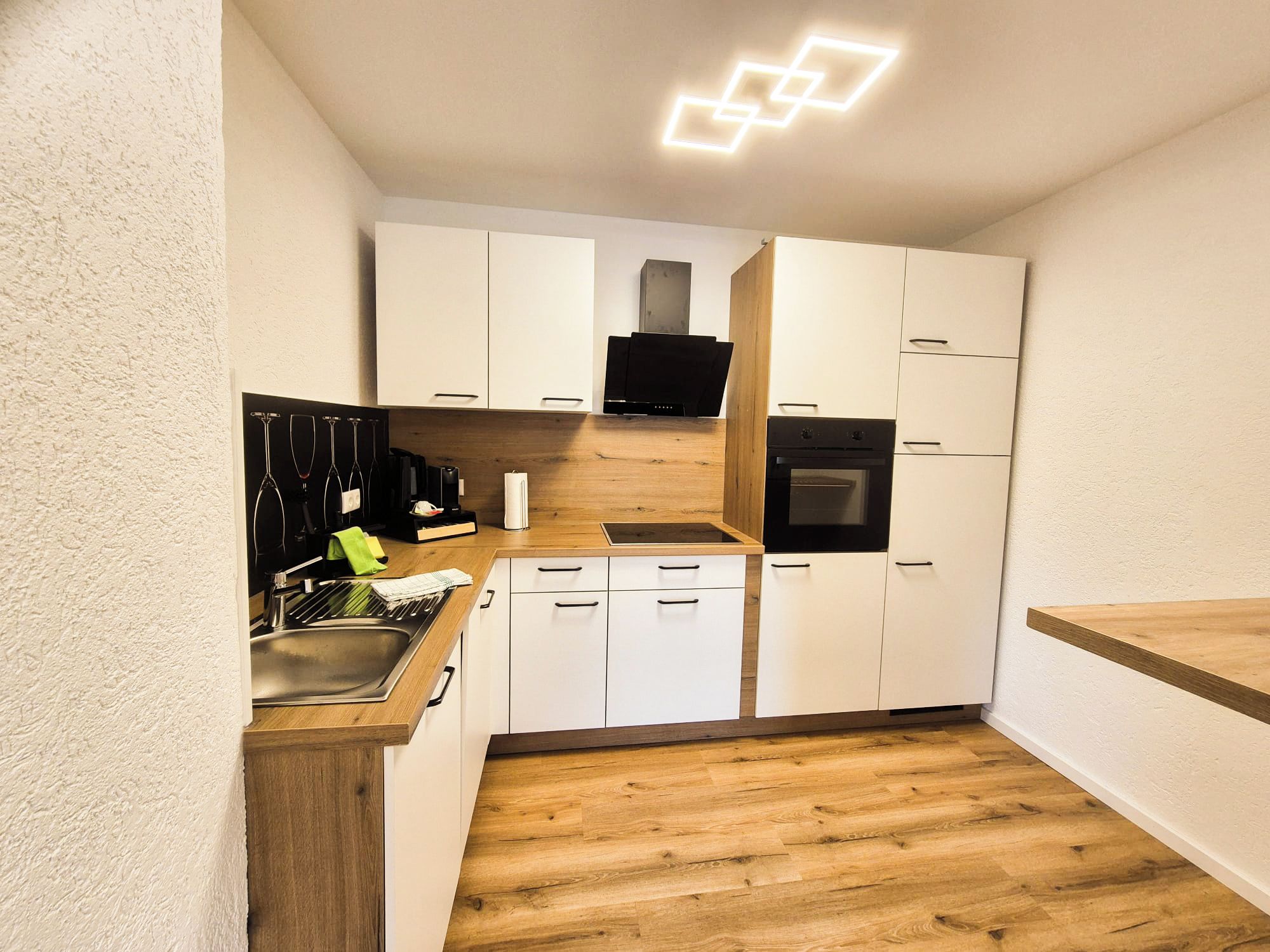 Een compacte keuken met witte kastjes, een houten aanrechtblad en een inbouwoven.