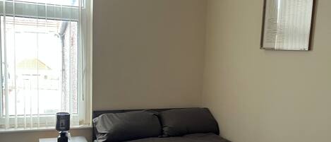 A bedroom with a bed, a nightstand, a window, and a framed picture on the wall.