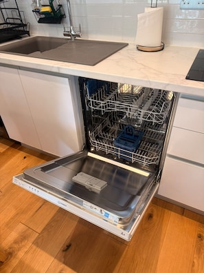 Un lave-vaisselle ouvert dans une cuisine dotée d’un plan de travail en marbre et d’un plancher en bois.