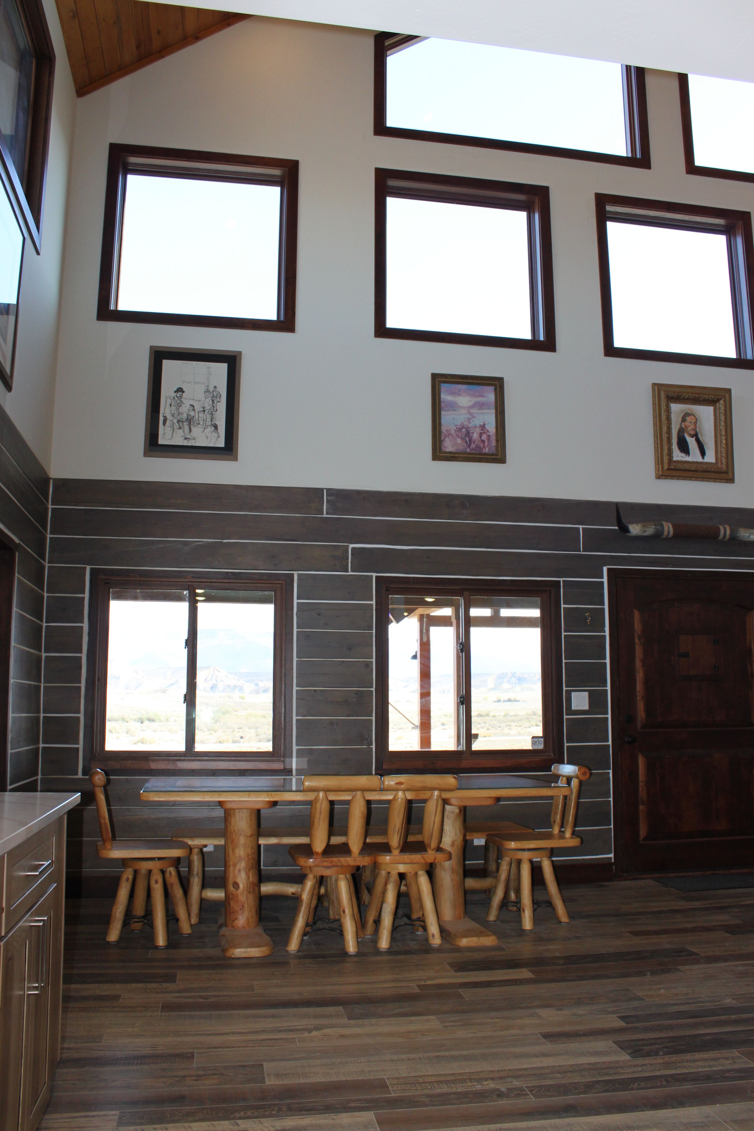 A spacious room with a high ceiling, multiple windows, and a dining area with wooden furniture.
